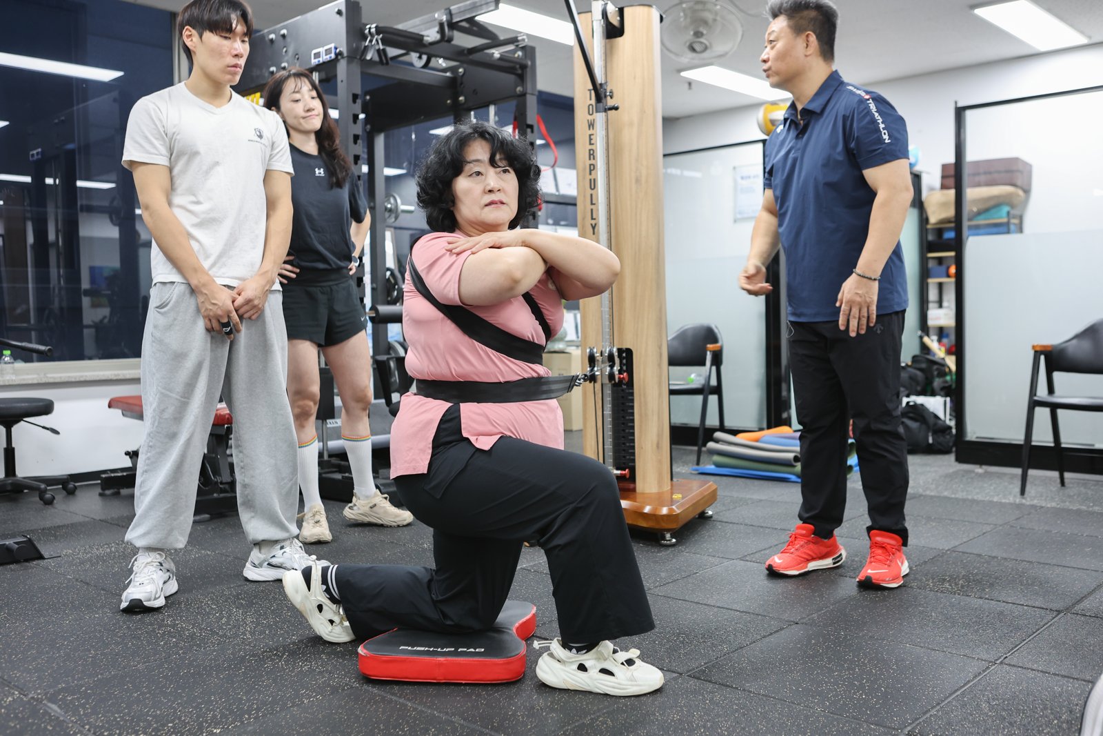 참여자가 무릎을 꿇은 자세로 타워풀리 스트랩을 몸에 걸고 회전 동작을 실습하는 장면